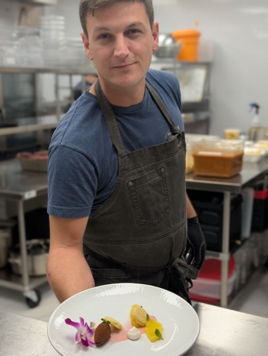 Justin in the galley holding a plated dessert