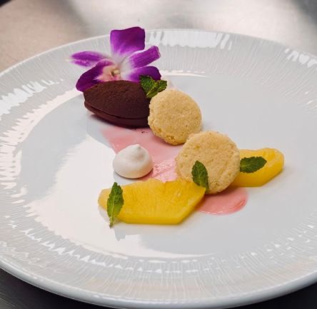 Dessert of chocolate quenelle, coconut tuiles and mango with an orchid